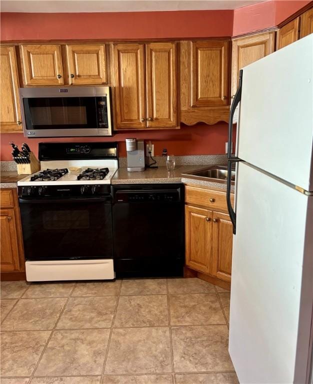 kitchen featuring stainless steel microwave, freestanding refrigerator, brown cabinetry, gas range, and dishwasher