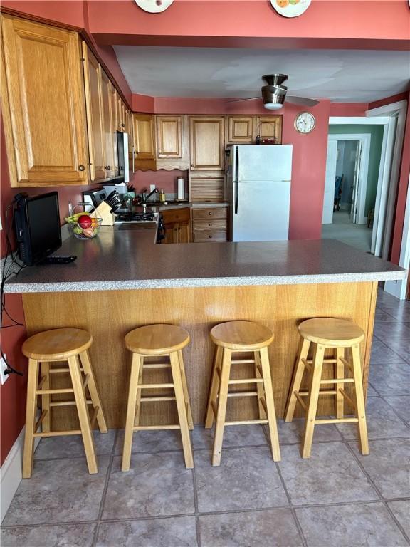 kitchen featuring a kitchen bar, dark countertops, freestanding refrigerator, a peninsula, and stove