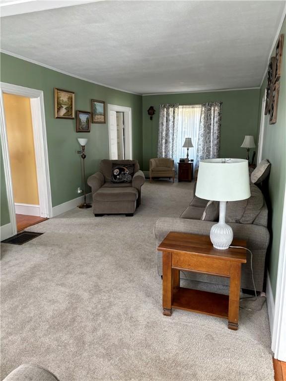 living area featuring visible vents, baseboards, carpet flooring, and crown molding