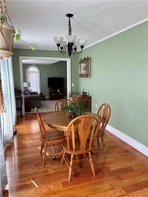 dining space featuring an inviting chandelier, wood finished floors, crown molding, and baseboards