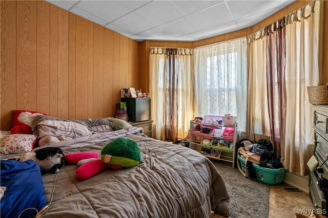 carpeted bedroom featuring a paneled ceiling and wood walls