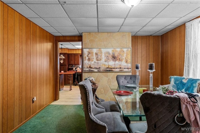 dining room featuring a paneled ceiling, wood walls, and carpet floors