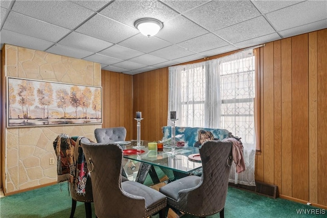 dining room featuring carpet, wood walls, and a paneled ceiling