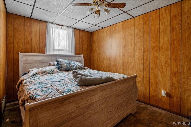 bedroom with wooden walls, a ceiling fan, and a drop ceiling