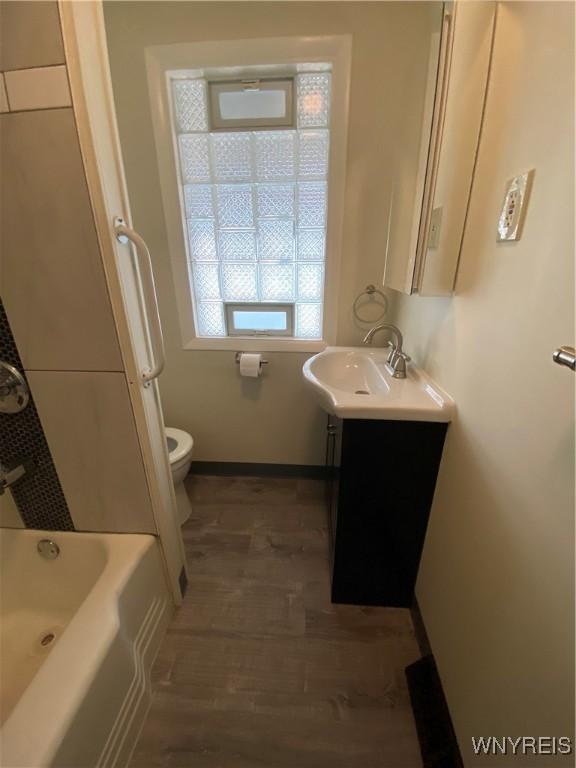 full bathroom with vanity, wood finished floors, a tub to relax in, baseboards, and toilet