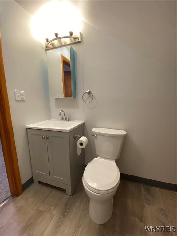 half bathroom with baseboards, toilet, wood finished floors, and vanity