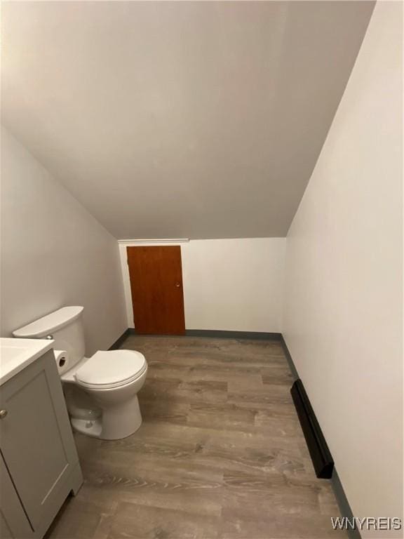 bathroom featuring toilet, lofted ceiling, wood finished floors, baseboards, and vanity