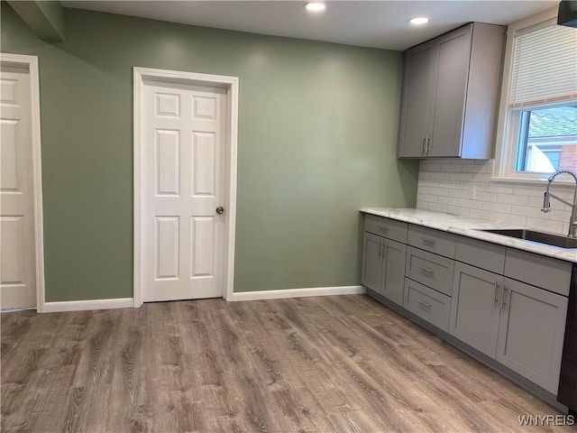 kitchen with light wood-type flooring, gray cabinetry, a sink, tasteful backsplash, and baseboards