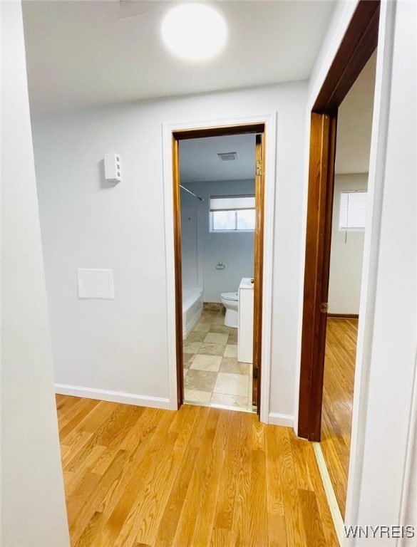 corridor with light wood-style floors, visible vents, and baseboards