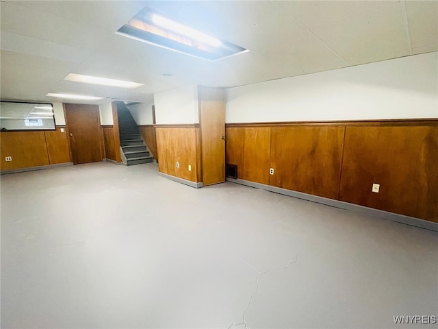 finished below grade area featuring stairs, a wainscoted wall, and wood walls