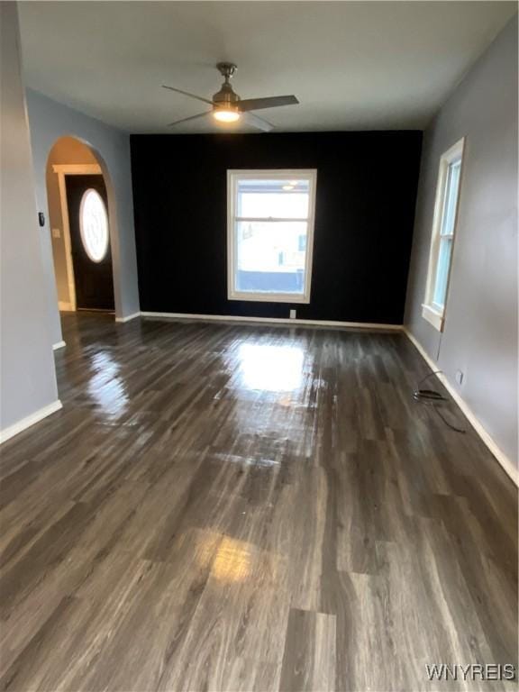 empty room with arched walkways, ceiling fan, baseboards, and wood finished floors