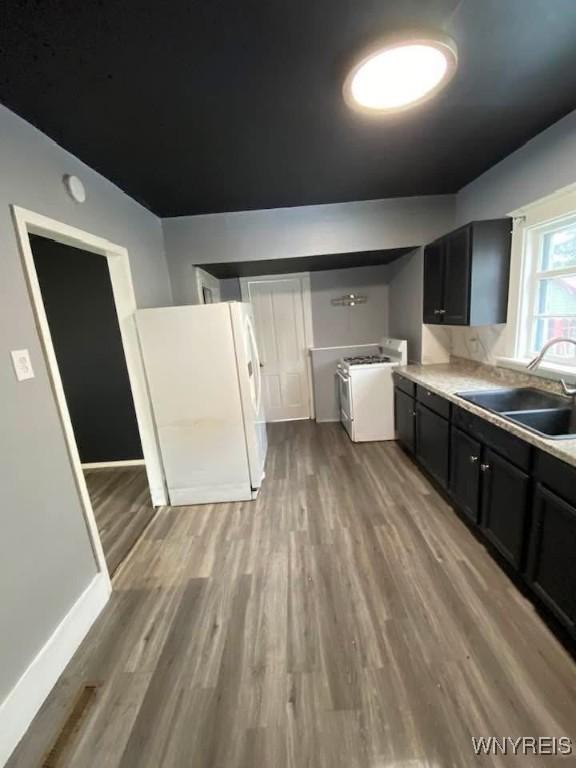 kitchen featuring light countertops, dark cabinetry, wood finished floors, white appliances, and a sink