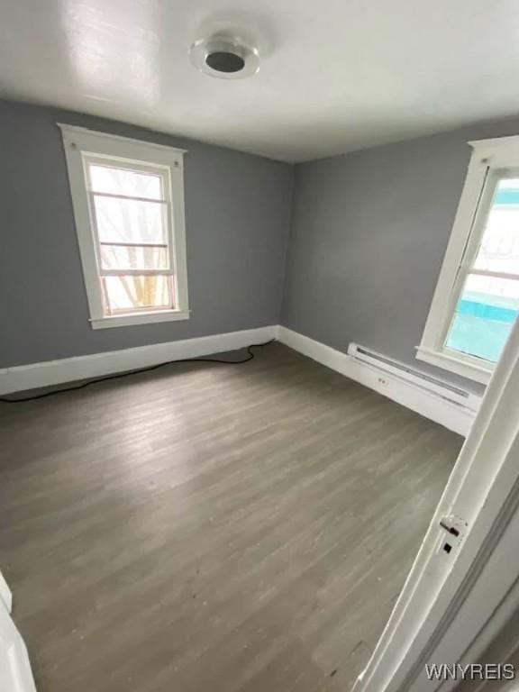 empty room with a baseboard heating unit, baseboards, and wood finished floors