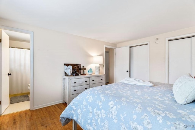 bedroom featuring light wood finished floors, two closets, ensuite bath, and baseboards