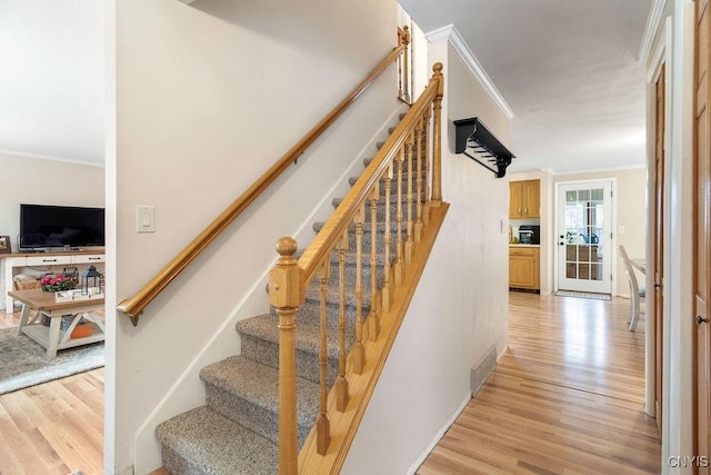 staircase with wood finished floors, visible vents, and ornamental molding