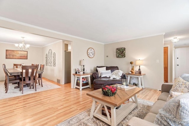 living room featuring ornamental molding, light wood-style floors, visible vents, and a chandelier