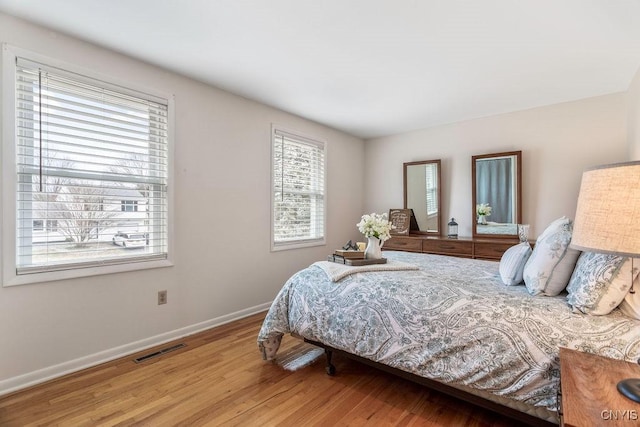 bedroom featuring visible vents, multiple windows, baseboards, and wood finished floors