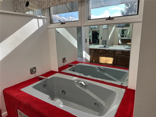 bathroom featuring a tub with jets, vanity, and a healthy amount of sunlight