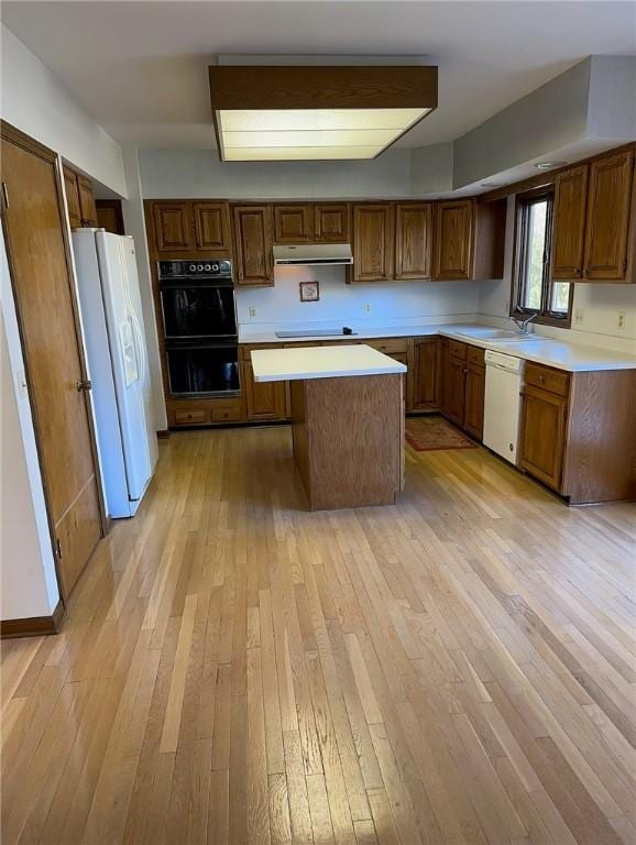 kitchen featuring a center island, under cabinet range hood, light countertops, light wood-style floors, and white appliances