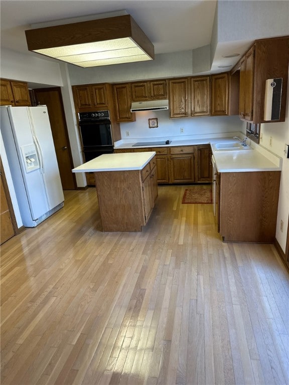 kitchen featuring light wood-type flooring, black appliances, range hood, brown cabinetry, and light countertops