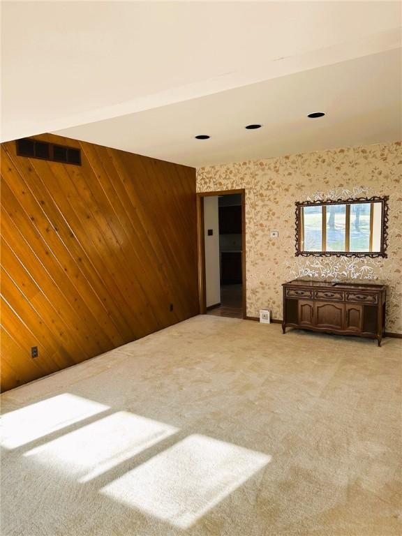 spare room featuring visible vents, light colored carpet, and wood walls