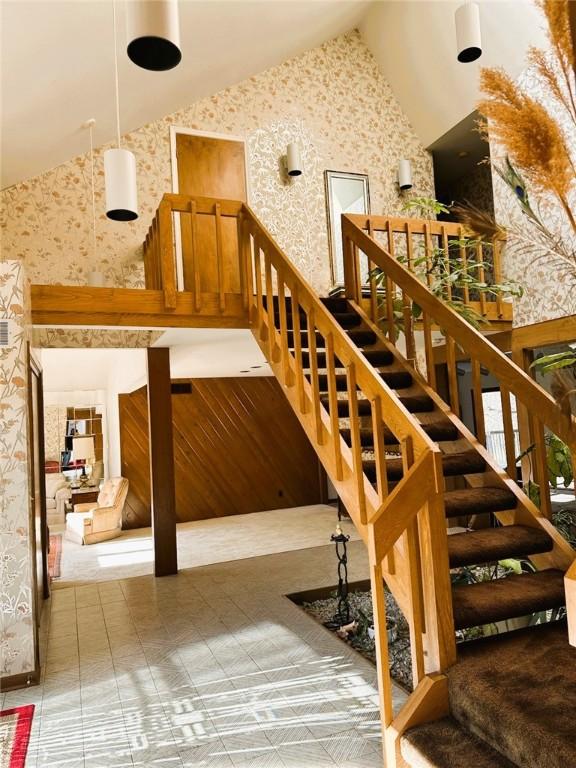 stairs featuring high vaulted ceiling and wallpapered walls