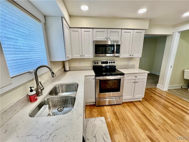 kitchen with baseboards, light stone counters, light wood-style floors, stainless steel appliances, and a sink