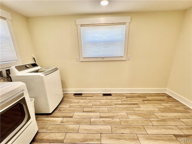 clothes washing area with wood finish floors, visible vents, independent washer and dryer, baseboards, and laundry area