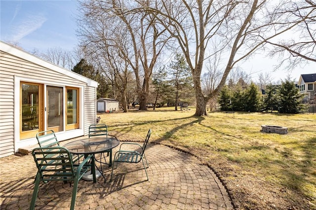 view of patio featuring an outbuilding, outdoor dining space, a fire pit, and a storage shed