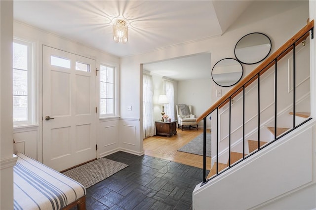 foyer with a decorative wall, wainscoting, stairs, and ornamental molding