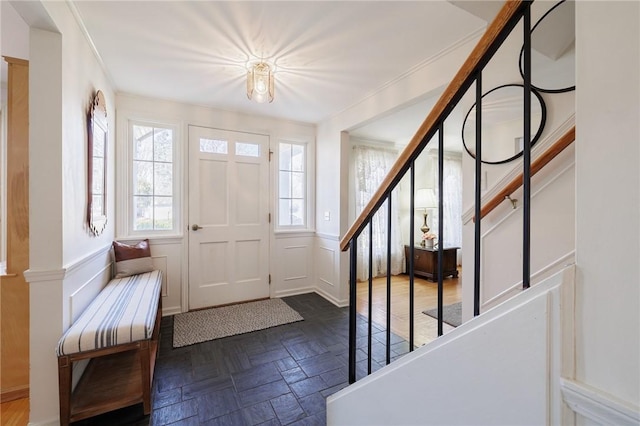 foyer entrance with stairway, a wainscoted wall, ornamental molding, and a decorative wall