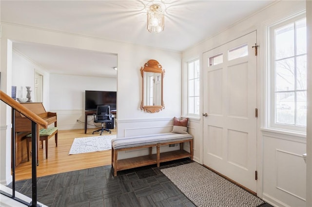 foyer entrance with a decorative wall, wainscoting, crown molding, and dark wood-type flooring