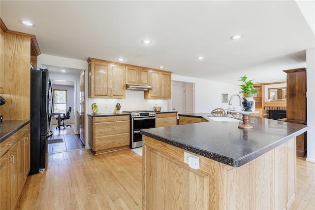 kitchen featuring dark countertops, under cabinet range hood, double oven range, freestanding refrigerator, and a sink