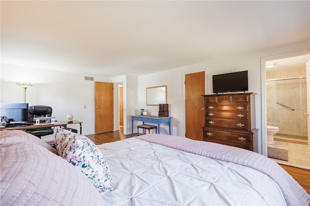 bedroom with connected bathroom, visible vents, and wood finished floors