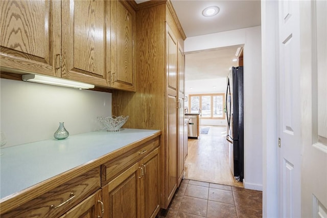 kitchen with brown cabinets, dark tile patterned floors, light countertops, and freestanding refrigerator