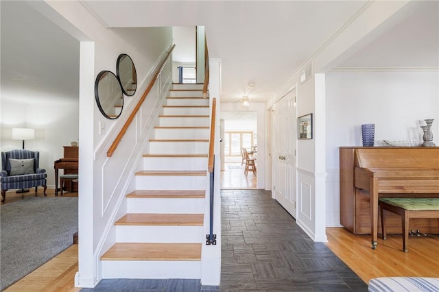 stairs with crown molding, wood finished floors, and visible vents