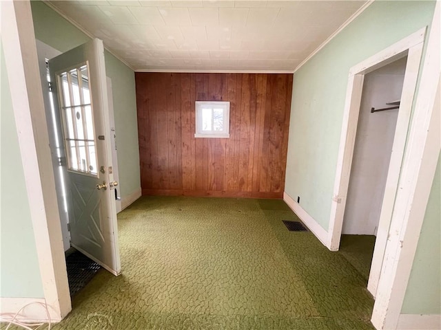 unfurnished bedroom with wooden walls, visible vents, baseboards, ornamental molding, and carpet flooring