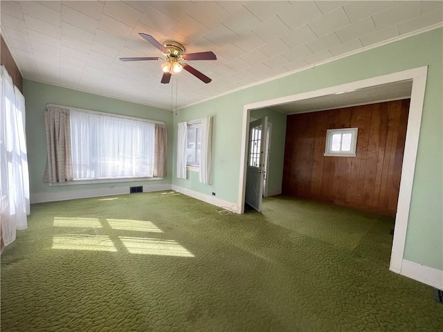 empty room with wooden walls, visible vents, baseboards, ornamental molding, and carpet flooring