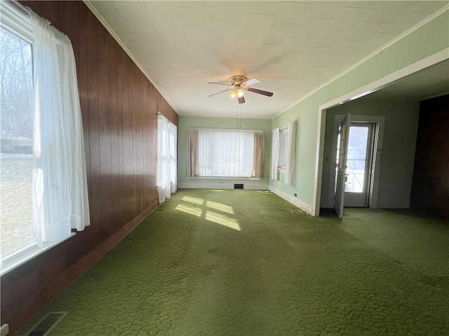 unfurnished room featuring visible vents, wooden walls, crown molding, light colored carpet, and ceiling fan