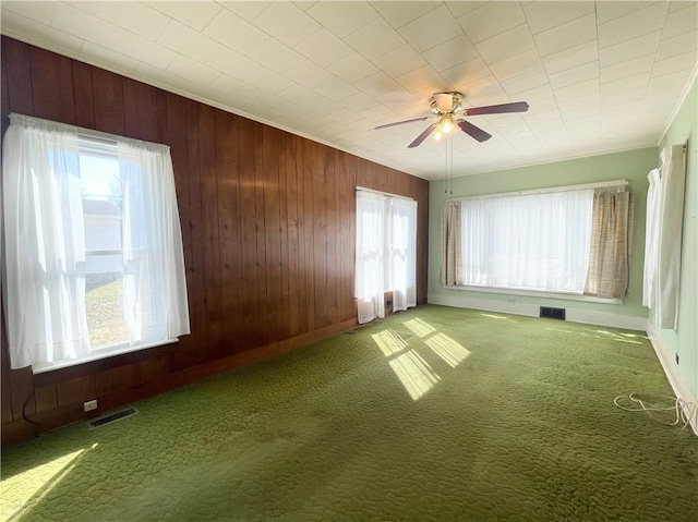 carpeted spare room featuring visible vents, wood walls, crown molding, and ceiling fan