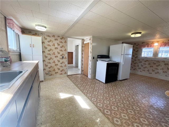 kitchen with wallpapered walls, light floors, freestanding refrigerator, electric stove, and a sink