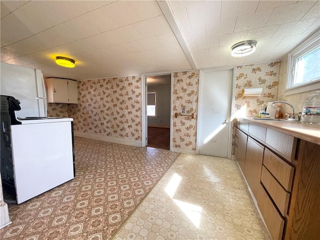 kitchen featuring stove, wallpapered walls, baseboards, and a sink