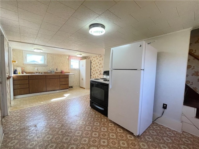 kitchen with black electric range, a sink, freestanding refrigerator, brown cabinetry, and light floors