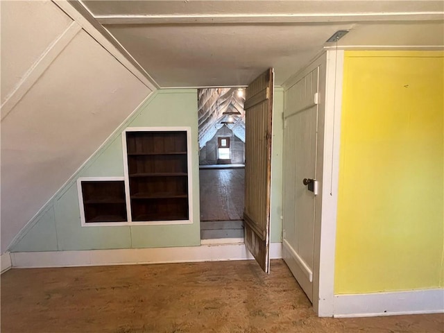 bonus room with built in shelves, concrete floors, and lofted ceiling