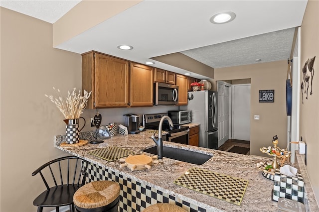 kitchen with a peninsula, a kitchen breakfast bar, brown cabinetry, stainless steel appliances, and a sink