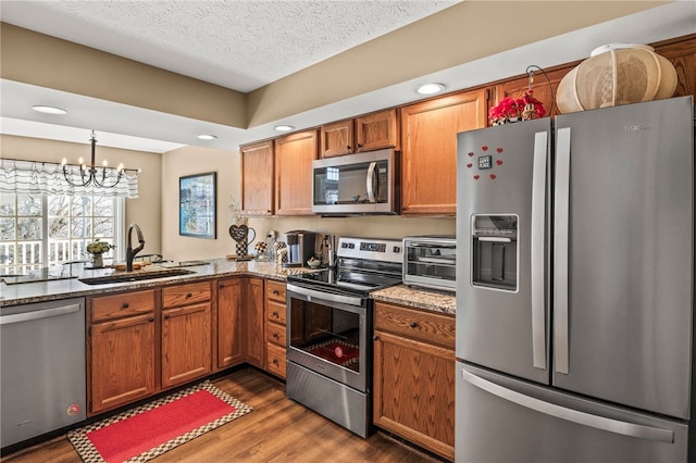 kitchen with a sink, stone countertops, stainless steel appliances, brown cabinetry, and dark wood-style flooring