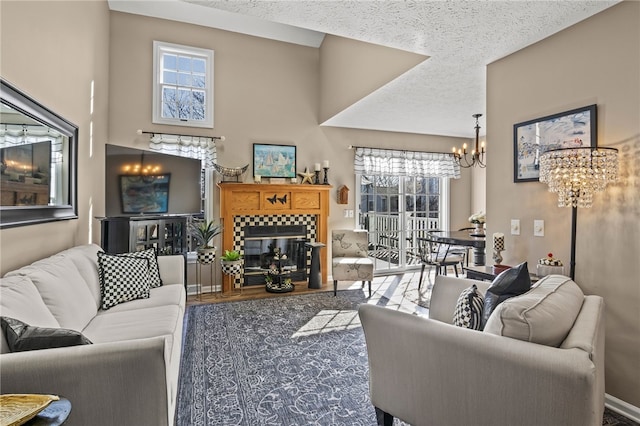 living room with a textured ceiling, wood finished floors, an inviting chandelier, baseboards, and a tile fireplace