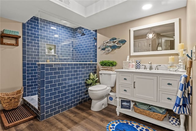 bathroom with visible vents, toilet, wood finished floors, tiled shower, and vanity