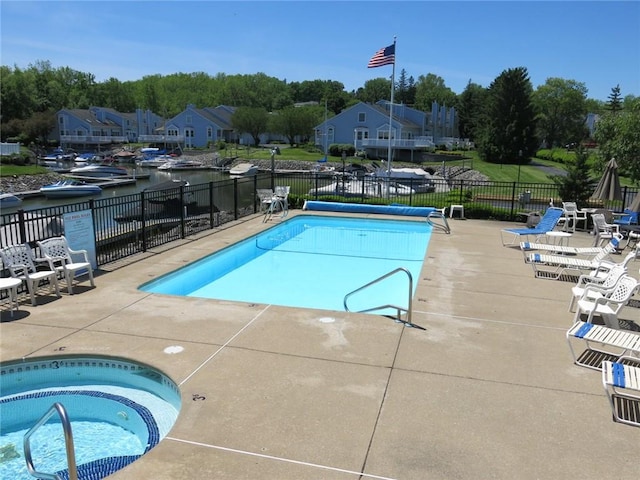 community pool with a patio area, fence, and a hot tub