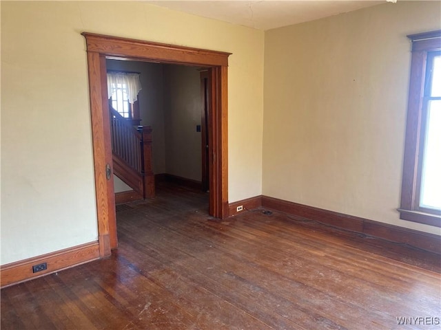 spare room featuring stairway, dark wood-type flooring, and baseboards